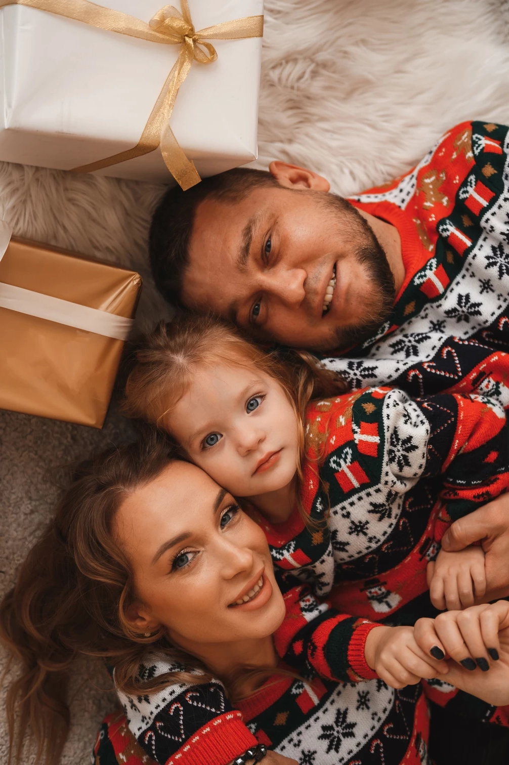 Сім'я в новорічних светрах позує для портрету на підлозі в подарунках.